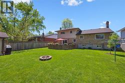 Expansive rear lawn featuring a stone-ringed fire pit, a private wood fence perimeter, and mature trees - 
