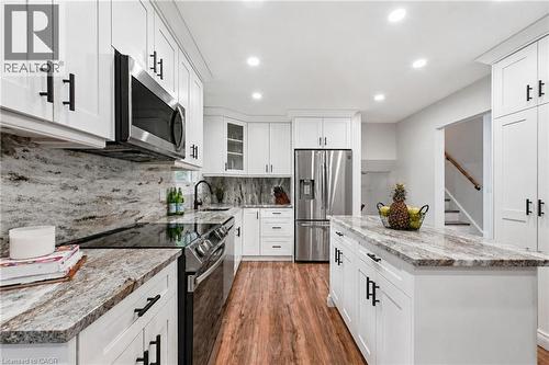 Bright kitchen featuring white shaker cabinetry with matte black hardware, stainless steel appliances, speckled stone countertops, and wood-finish flooring - 76 Lower Canada Crescent, Kitchener, ON - Indoor Photo Showing Kitchen With Upgraded Kitchen