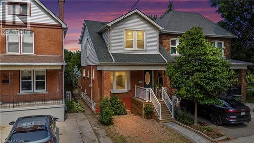 Brick facade home featuring a gabled roofline, front porch with white railings, and a paved driveway - 37 Park Row N, Hamilton, ON - Outdoor