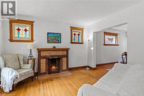 Living room featuring a brick and tile fireplace, wood-finish flooring, and multiple stained-glass windows with wood trim - 37 Park Row N, Hamilton, ON - Indoor Photo Showing Living Room With Fireplace