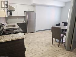 Kitchen with freestanding refrigerator, under cabinet range hood, light stone countertops, light wood-style flooring, and freestanding range oven - 