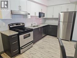 Kitchen featuring stainless steel appliances, under cabinet range hood, light wood-type flooring, white cabinets, and light stone counters - 
