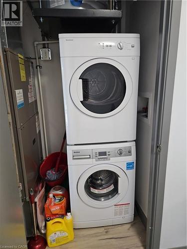 Washroom featuring stacked washer / drying machine, heating unit, and wood finished floors - 258B Sunview Street Unit# 255, Waterloo, ON - Indoor Photo Showing Laundry Room