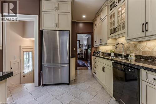 Galley kitchen featuring light-toned cabinetry, stainless steel refrigerator, black dishwasher, dark countertops, and a tiled backsplash - 569 Locust Street, Burlington, ON - Indoor Photo Showing Kitchen With Double Sink