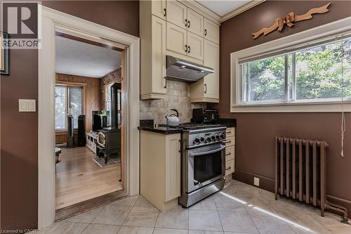 Kitchen area featuring light-toned cabinetry with dark hardware, a stainless steel range with overhead ventilation, dark countertops, and a tiled backsplash - 569 Locust Street, Burlington, ON - Indoor Photo Showing Kitchen