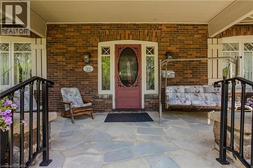 Brick exterior with a stone patio, featuring a carved front door with glass insert, white window trim, and black metal railings - 569 Locust Street, Burlington, ON - Outdoor With Deck Patio Veranda With Exterior