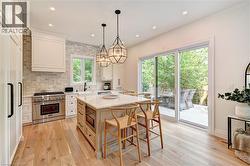 Spacious kitchen featuring an expansive central island, stainless steel range, light wood-finish flooring, and direct access to an outdoor deck through sliding glass doors - 