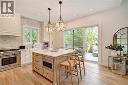 Bright kitchen featuring a substantial central island with integrated microwave, stone countertop, and two pendant light fixtures - 