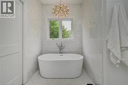 Freestanding soaking tub with a floor-mounted faucet set against marble-look tile walls - 
