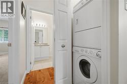 Hallway with stackable washer and dryer unit, wood-finish flooring, and a bathroom featuring a white vanity with a light-colored countertop and a wall-mounted light fixture - 
