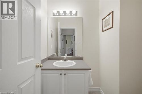 Vanity with an integrated sink, a gray countertop, white base cabinetry with brushed nickel hardware, and an overhead four-bulb light fixture - 34 Southbrook Drive Unit# 13, Binbrook, ON - Indoor Photo Showing Bathroom