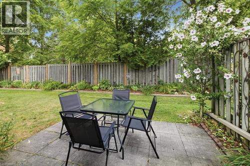 Paved patio area featuring a manicured lawn, full privacy fencing, mature trees, and established flowering shrubs - 34 Southbrook Drive Unit# 13, Binbrook, ON - Outdoor With Backyard