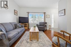 Living area with wood-finish flooring, white walls, and a large window with white plantation shutters - 