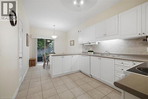 Kitchen featuring white cabinetry, light-toned countertops, a diagonal tile backsplash, and tile flooring - 34 Southbrook Drive Unit# 13, Binbrook, ON - Indoor Photo Showing Kitchen With Double Sink