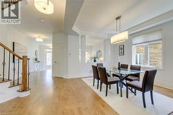Open-concept dining area featuring wood-finish flooring, a contemporary chandelier, and natural light from a large window - 