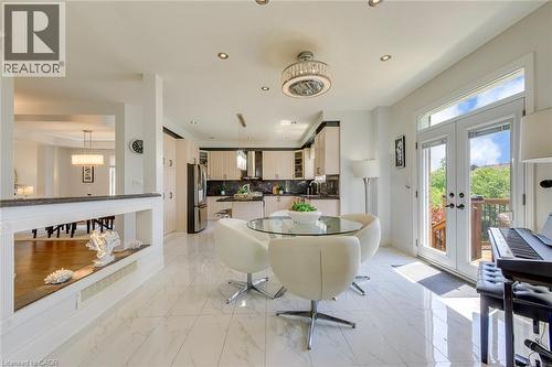Bright eat-in kitchen area featuring white marble-look tile flooring, a contemporary ceiling fixture, recessed lighting, and double glass-paneled doors with transom windows - 2380 Woodcrest Drive, Oakville, ON - Indoor Photo Showing Other Room With Fireplace