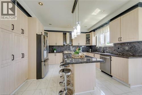 Contemporary kitchen featuring a central island with counter seating, light wood-finish cabinetry, dark stone countertops, stainless steel appliances, and recessed lighting - 2380 Woodcrest Drive, Oakville, ON - Indoor Photo Showing Kitchen With Upgraded Kitchen