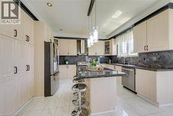 Contemporary kitchen featuring a central island with counter seating, light wood-finish cabinetry, dark stone countertops, stainless steel appliances, and recessed lighting - 