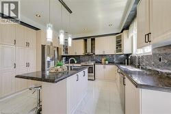 Contemporary kitchen featuring cream-toned cabinetry, dark stone countertops, stainless steel appliances, a center island with pendant lighting, and white tile flooring - 