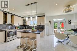 Contemporary kitchen featuring light wood-finish cabinetry, dark stone countertops and backsplash, stainless steel appliances, and a central island with pendant lighting - 