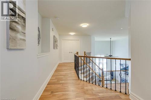 Upper-level hallway featuring wood-finish flooring, white baseboards, and a railing with dark metal spindles and a wood-finish top rail - 2380 Woodcrest Drive, Oakville, ON - Indoor Photo Showing Other Room