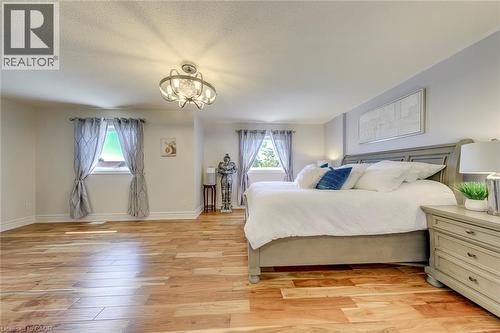Spacious room featuring wood-finish flooring, two windows with curtain rods, and a decorative ceiling light fixture - 2380 Woodcrest Drive, Oakville, ON - Indoor Photo Showing Bedroom