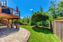 Spacious backyard featuring a paver patio with decorative stone pillars, a manicured lawn, and a mature tree - 