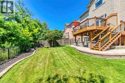 Expansive backyard featuring a manicured lawn, a multi-level wood deck with stairs, and a stone patio - 