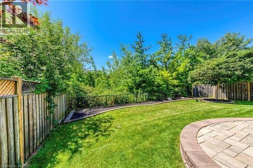 Expansive backyard featuring a paver patio with a curved stone retaining wall, lush green lawn, wood privacy fencing, and mature perimeter trees - 2380 Woodcrest Drive, Oakville, ON - Outdoor