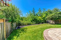 Expansive backyard featuring a paver patio with a curved stone retaining wall, lush green lawn, wood privacy fencing, and mature perimeter trees - 