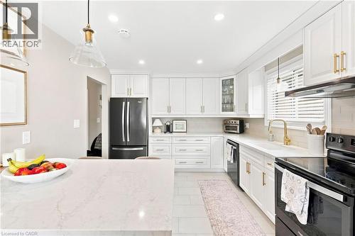 Modern kitchen featuring white shaker cabinetry, gold-tone hardware, a black French door refrigerator, and a white countertop island - 15 Quay Court, Hamilton, ON - Indoor Photo Showing Kitchen
