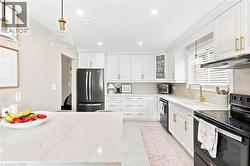 Modern kitchen featuring white shaker cabinetry, gold-tone hardware, a black French door refrigerator, and a white countertop island - 