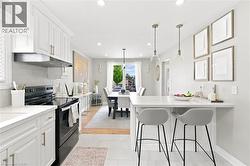 Open-concept kitchen featuring white shaker cabinetry, an integrated range hood, and a white subway tile backsplash - 