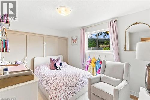 Bright room with a built-in wall unit, a framed window with curtains, and a ceiling-mounted light fixture - 15 Quay Court, Hamilton, ON - Indoor Photo Showing Bedroom
