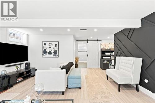 Light wood-finish flooring throughout, recessed ceiling lighting, a dark accent wall with geometric paneling, and a white barn door with black hardware - 15 Quay Court, Hamilton, ON - Indoor Photo Showing Other Room