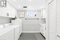 Laundry room with white shaker-style cabinetry, dark tile flooring, and a window - 