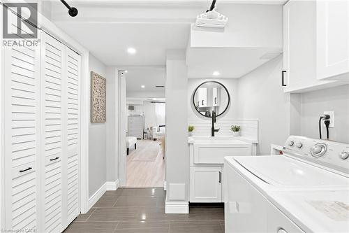 Dedicated laundry area featuring a white farmhouse sink with a matte black faucet, subway tile backsplash, and overhead cabinetry - 15 Quay Court, Hamilton, ON - Indoor Photo Showing Laundry Room