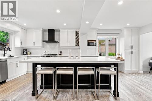 Spacious kitchen featuring an expansive center island with seating, white cabinetry, integrated range hood, built-in wine rack, and wood-finish flooring - 10 Rolling Acres Drive, Kitchener, ON - Indoor