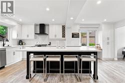 Spacious kitchen featuring an expansive center island with seating, white cabinetry, integrated range hood, built-in wine rack, and wood-finish flooring - 