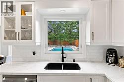 White shaker-style cabinetry with glass-front accents, white subway tile backsplash, and a black undermount sink with a matte black faucet - 