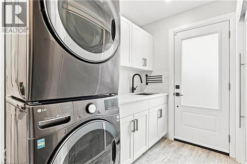 Stackable laundry appliances with a side-by-side washer and dryer, complemented by white cabinetry, a black faucet, and a frosted glass panel door - 10 Rolling Acres Drive, Kitchener, ON - Indoor Photo Showing Laundry Room