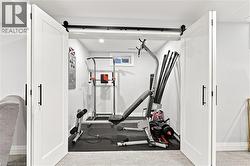 Dedicated exercise space featuring white barn doors with black hardware, a high transom window, light gray walls, and dark rubber flooring - 