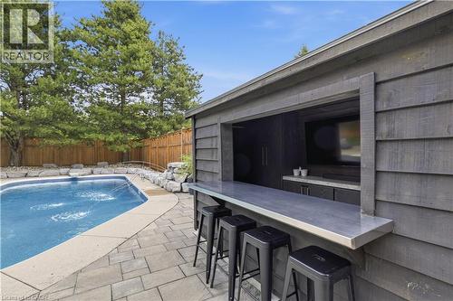 Outdoor bar area featuring a pass-through window with a metal countertop, built-in cabinetry, and a dedicated entertainment space - 10 Rolling Acres Drive, Kitchener, ON - Outdoor With In Ground Pool With Deck Patio Veranda