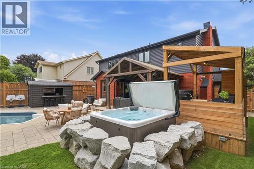 Backyard oasis featuring a built-in hot tub, an in-ground swimming pool, a dedicated outdoor bar structure, paver patio, and a covered wooden deck - 10 Rolling Acres Drive, Kitchener, ON - Outdoor With Deck Patio Veranda