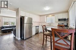 Kitchen featuring wood-finish flooring, white cabinetry, stainless steel appliances, and a tiled backsplash - 