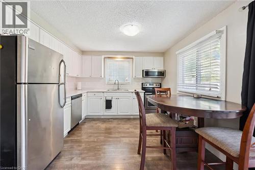 Kitchen featuring wood-finish flooring, white cabinetry, stainless steel appliances, and a window with horizontal blinds - 589 Elgin Street N, Cambridge, ON - Indoor