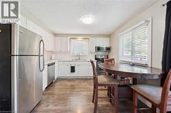 Kitchen featuring wood-finish flooring, white cabinetry, stainless steel appliances, and a window with horizontal blinds - 