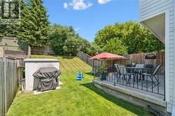 Spacious backyard featuring a concrete patio with black metal railings, a manicured lawn, an outdoor storage shed, and mature trees providing natural screening - 