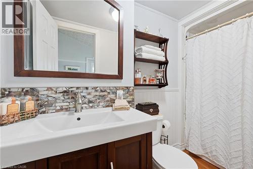 Bathroom featuring a dark wood framed mirror, a vanity with a white rectangular sink, mosaic tile backsplash, a toilet, and beadboard paneling - 153 Montrose Street N, Cambridge, ON - Indoor Photo Showing Bathroom