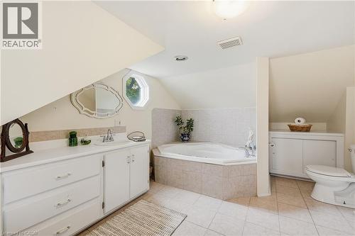 Bathroom featuring a corner built-in tub with tile surround, a single vanity with storage cabinetry and drawers, an octagonal window, and tiled flooring - 153 Montrose Street N, Cambridge, ON - Indoor Photo Showing Bathroom